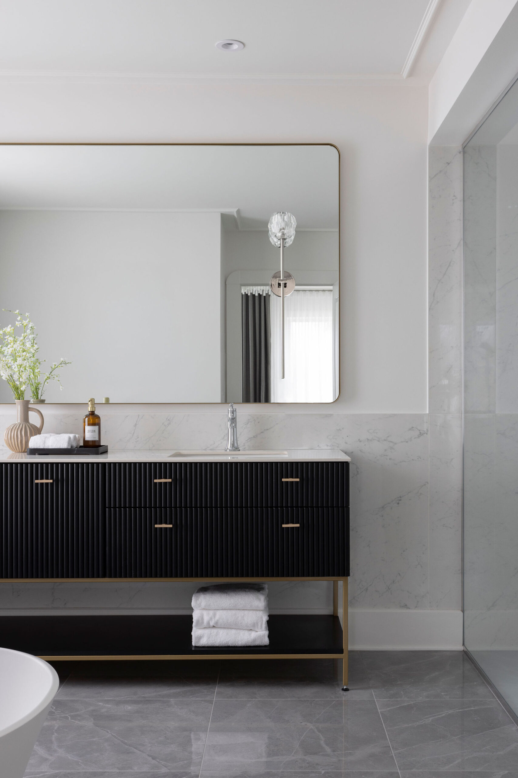 Salle de bain des maîtres avec meuble-lavabo noir, comptoir blanc, grand miroir, murs clairs et ambiance épurée.