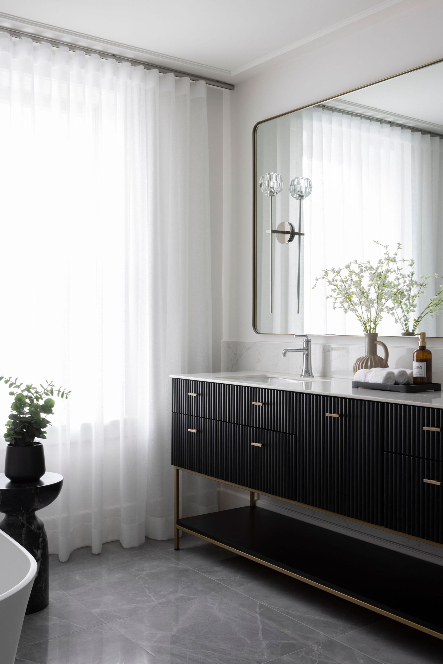 Salle de bain des maîtres avec meuble-lavabo noir, comptoir blanc, grand miroir, murs clairs et ambiance épurée.