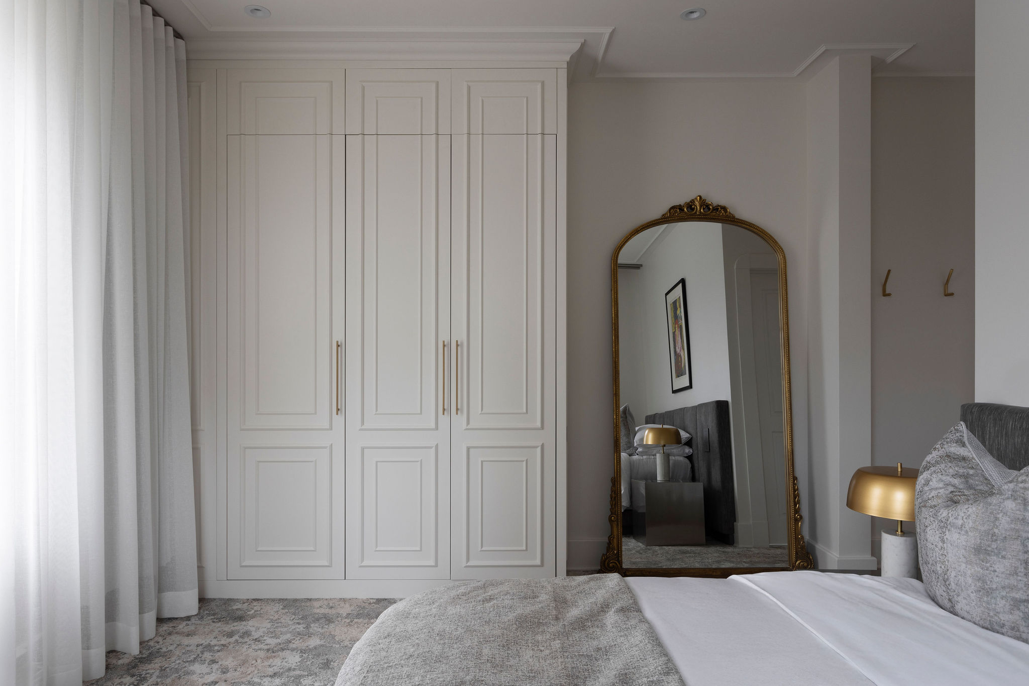 Chambre avec portes de rangement blanches, grand miroir arqué, tapis à motif doux et ambiance lumineuse.