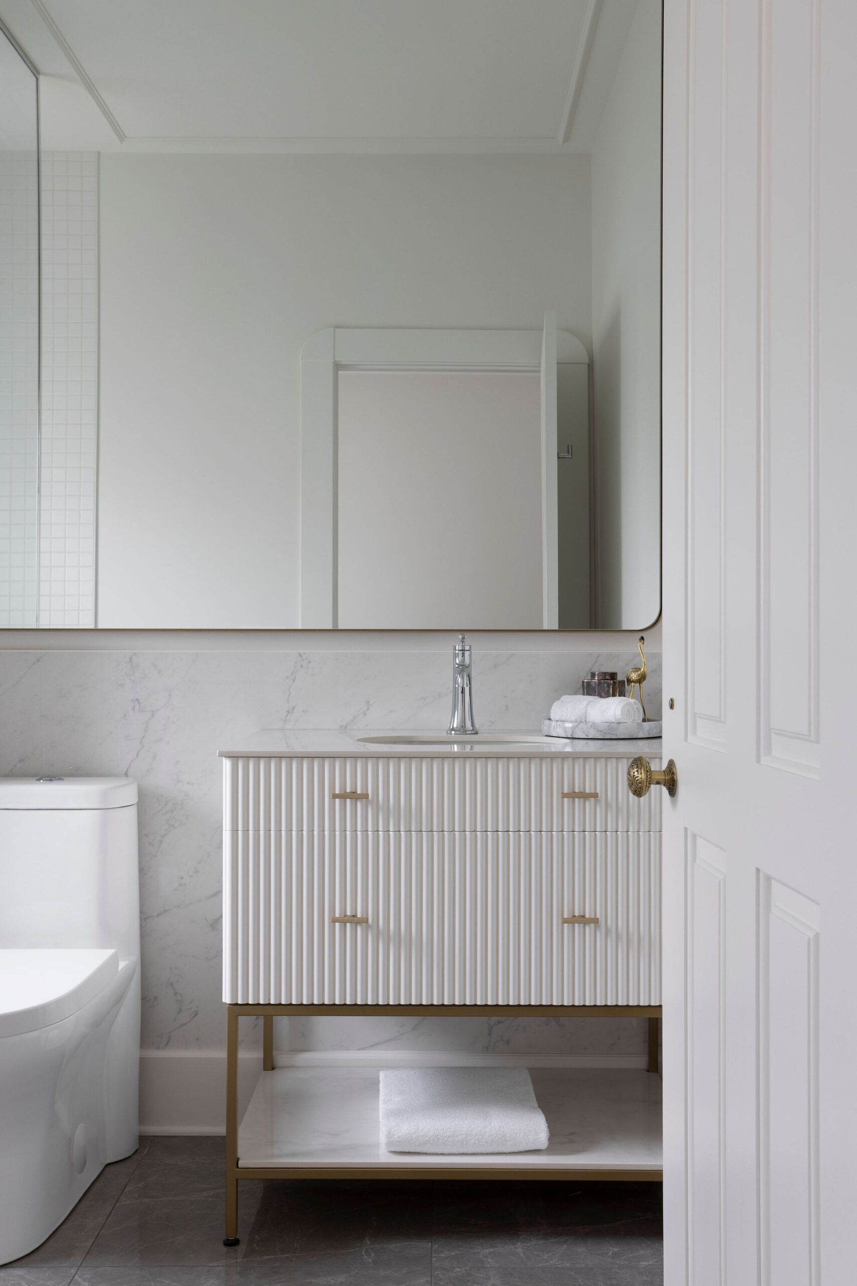 Salle de bain avec meuble-lavabo clair, comptoir blanc, miroir mural, robinetterie dorée et ambiance lumineuse.