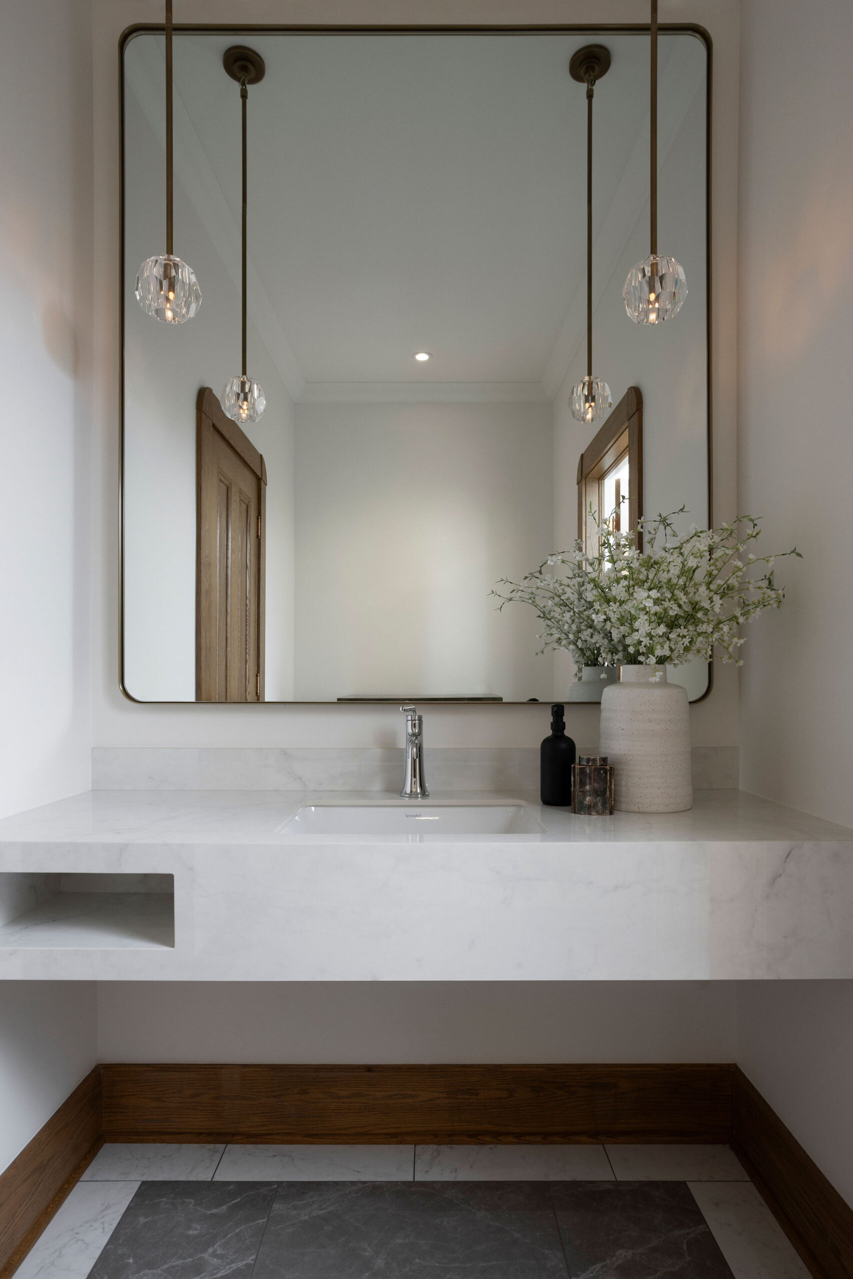 Salle d’eau lumineuse avec meuble-lavabo blanc, miroir mural, robinetterie dorée, comptoir clair et bouquet décoratif.