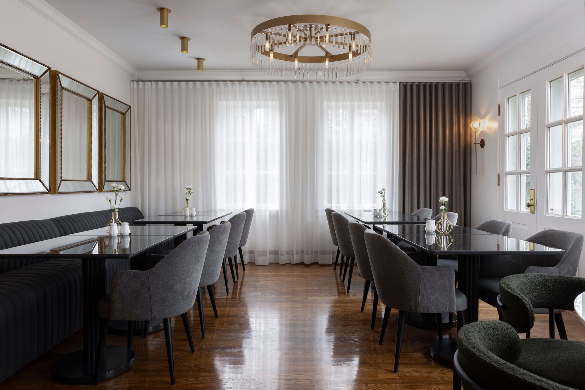 Coin repas lumineux avec table ronde blanche, banquette foncée, chaises noires, voilages blancs et moulures murales.